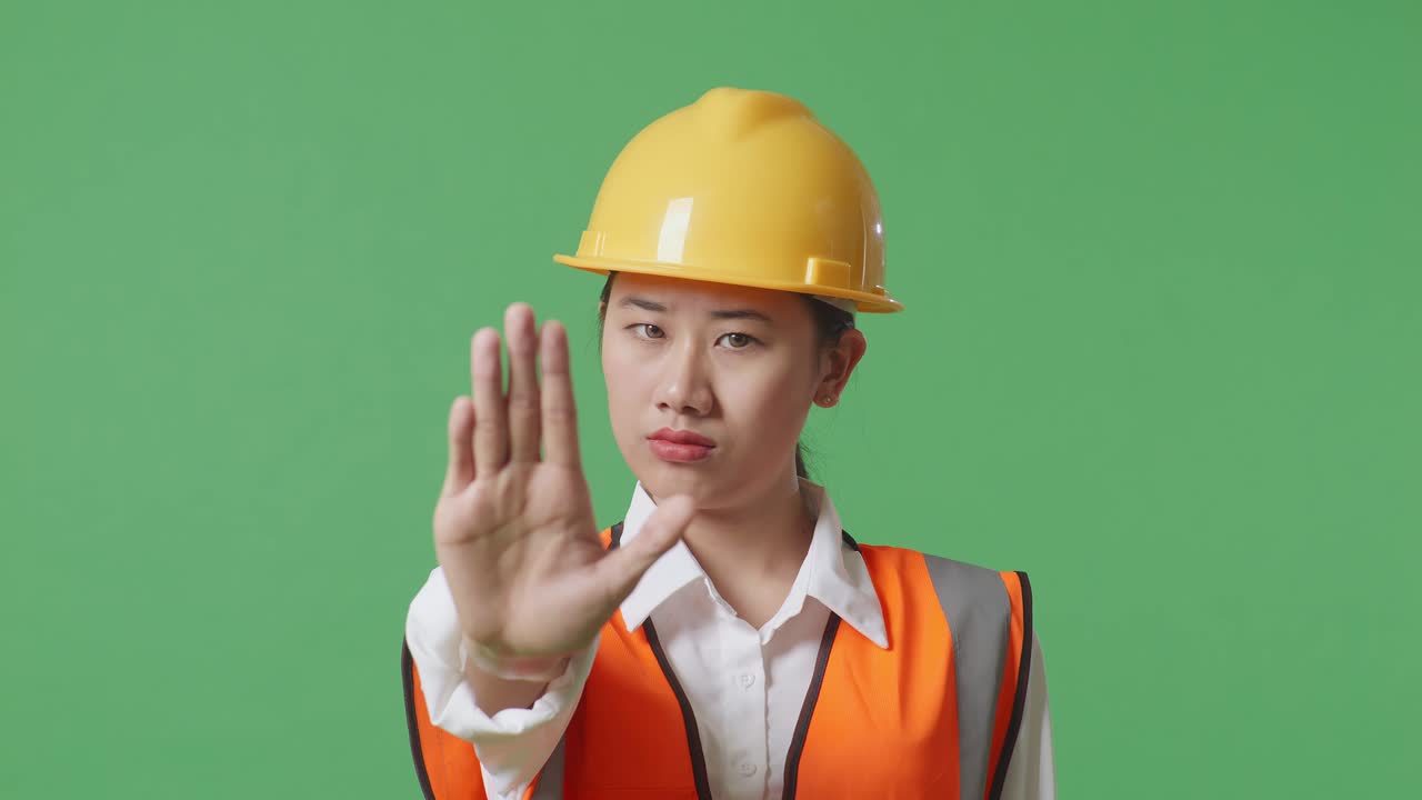 Close Up Of Asian Female Engineer With Safety Helmet Disapproving With No Hand Sign While Standing In The Green Screen Background Studio