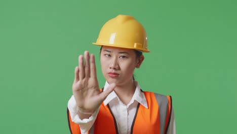 close up of asian female engineer with safety helmet disapproving with no hand sign while standing in the green screen background studio