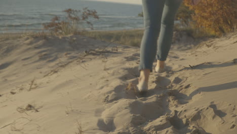 handheld shot at ground level following a young woman walking through sand dunes at sunset.  shot in 4k