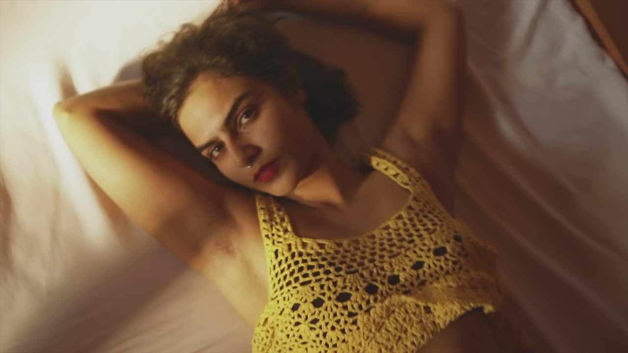 섹시한 아시아 여성 모델의 얼굴 클로즈업 샷, 실내 침대에 매혹적으로 누워 있는 그녀를 드러내기 위해 돌리기