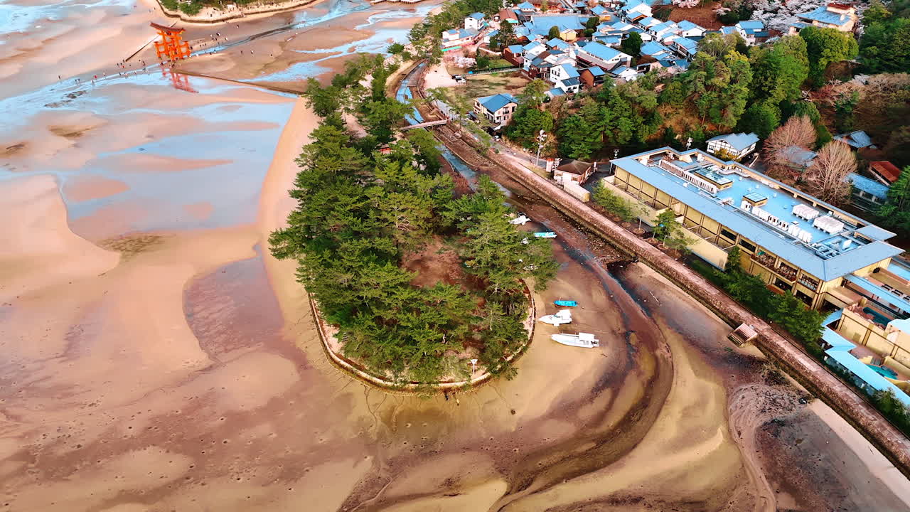 Multiple lovely houses surround the territory of sacred Itsukushima Shrine at the Miyajima island, Japan. Period of low tide at the sandy shore of the Inland Sea. Aerial view.