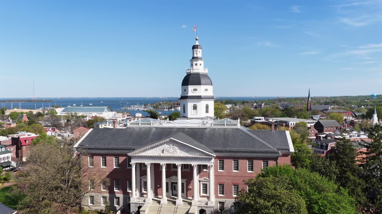 Dronebilde fra luften av Maryland State House i Annapolis, Maryland, USA om våren med blå himmel, historisk mursteinskapitolbygning, hvite søyler, kuppelarkitektur og Chesapeake Bay i bakgrunnen. Stigende