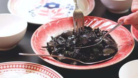 person serving squid dish with black ink sauce in phuket, thailand