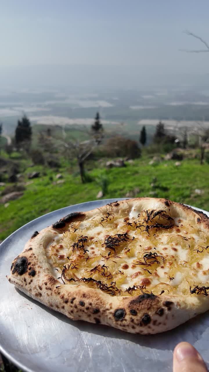 La pizza napoletana immersa nella natura crea una composizione perfetta, mentre il piatto artigianale viene tenuto sopra una pittoresca valle agricola