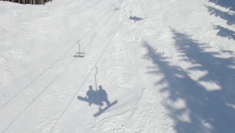 shadow of two snowboarders in the snow - ski lift approaching drop off at ski resort - bright sunshine - beautiful weather - smooth 4k footage