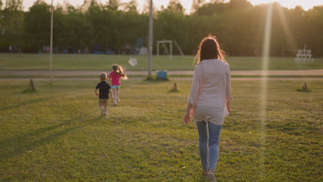 woman with little children walks to sports ground at sunset