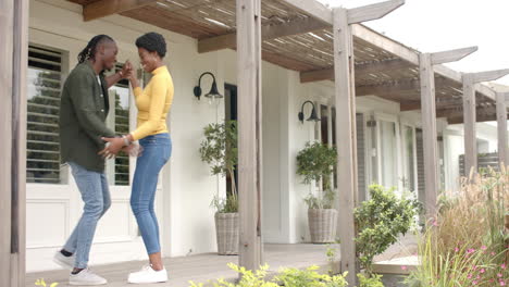 smiling african american couple holding keys, celebrating new home ownership on porch
