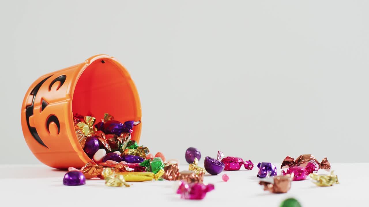 espeluznante balde impreso de calabaza de halloween lleno de dulces que caen contra un fondo gris