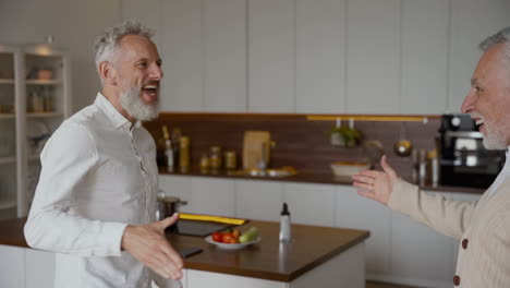 two happy senior men friends greeting each other with a hug and talking at home