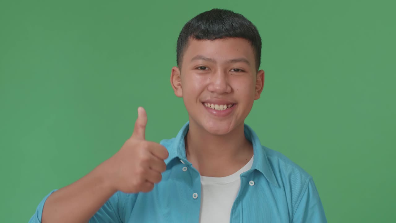 Happy Young Asian Boy Showing Thumbs Up Gesture While Standing In The Green Screen Studio