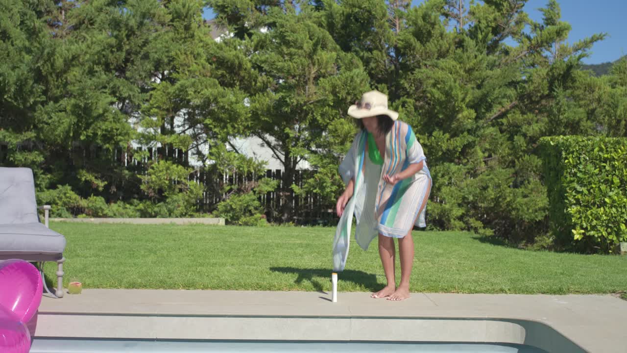 Adult African-American woman in hat applying SPF pre-swim walking to pool in warm yard, copy space