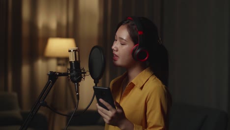 female singer holding and looking smart phone while singing in home studio