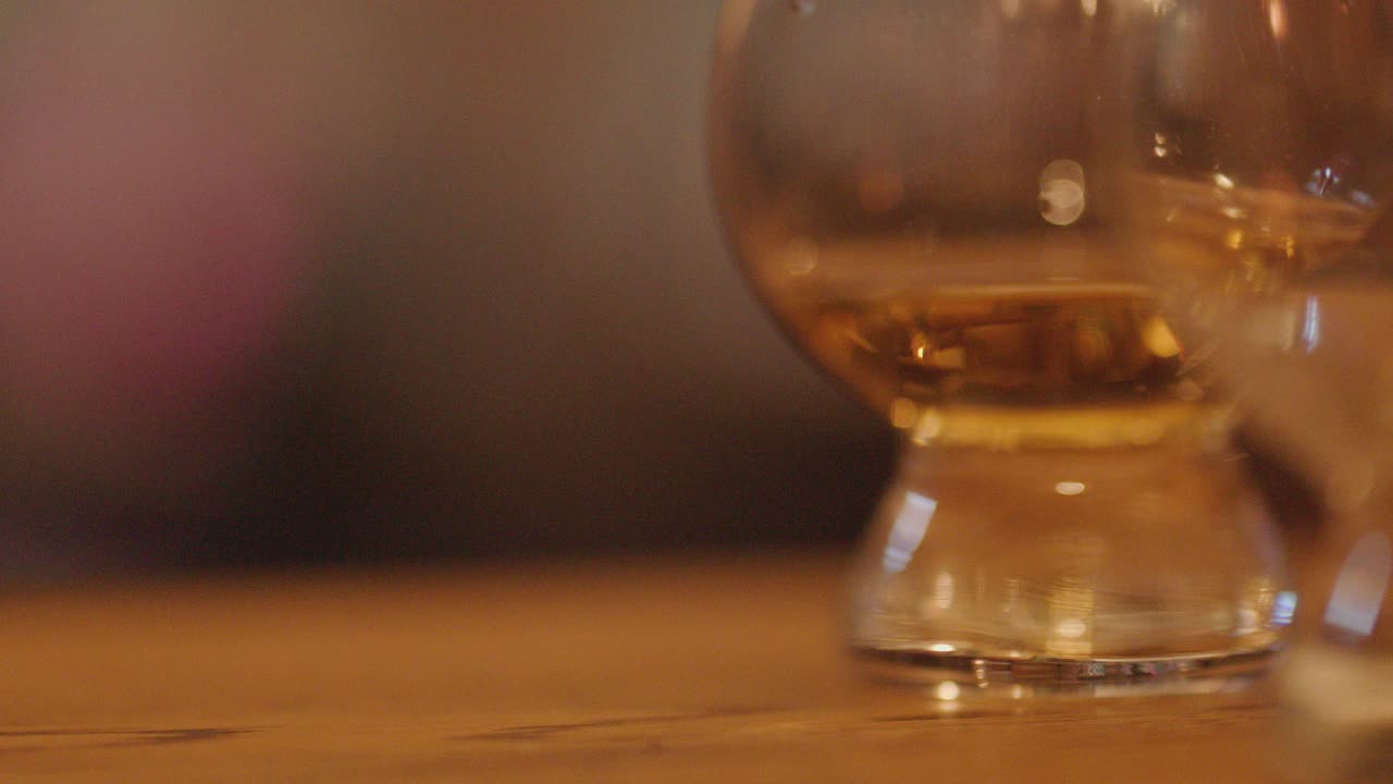 Close-up of whiskey glasses on wooden bar, hand reaching in warm, inviting lighting