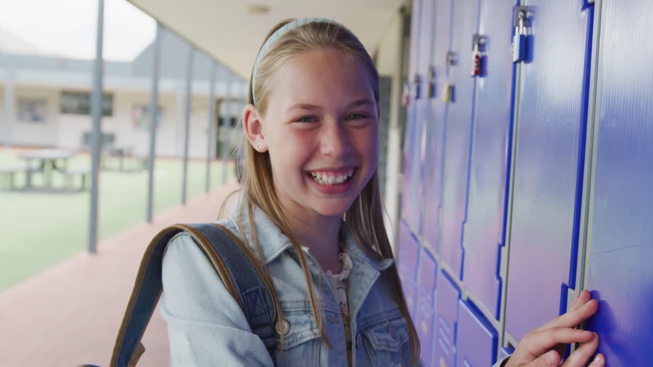 retrato de video de una estudiante caucásica feliz usando un casillero en el pasillo de la escuela, espacio de copia
