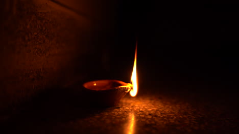 a clay candle diya burning brightly in one corner of a dark room, symbol of diwali the indian festival of light