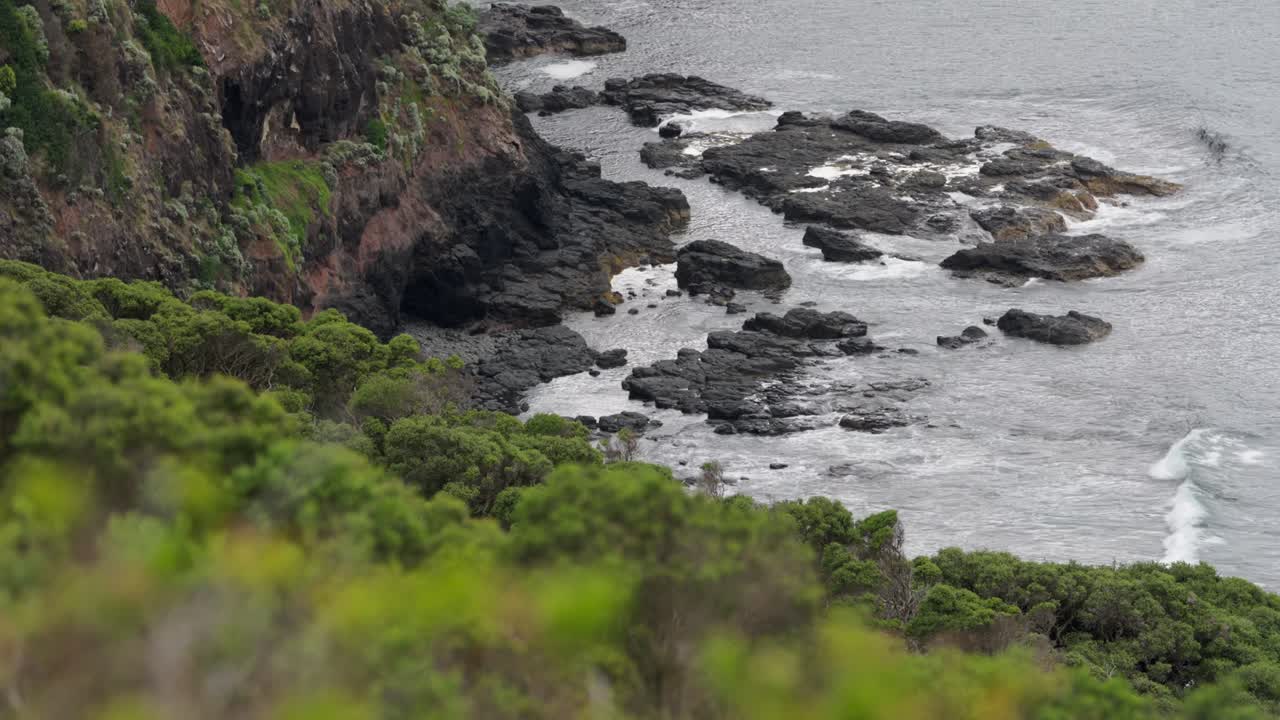 Waves crashing powerfully against the base of towering cliffs, with water splashing and foam rising in a dramatic display of nature’s force.