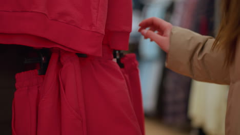 close-up shot of a hand in a brown jacket reaching for a red garment in a clothing store. the texture and detail of the red fabric, as well as the casual action of browsing through clothing racks