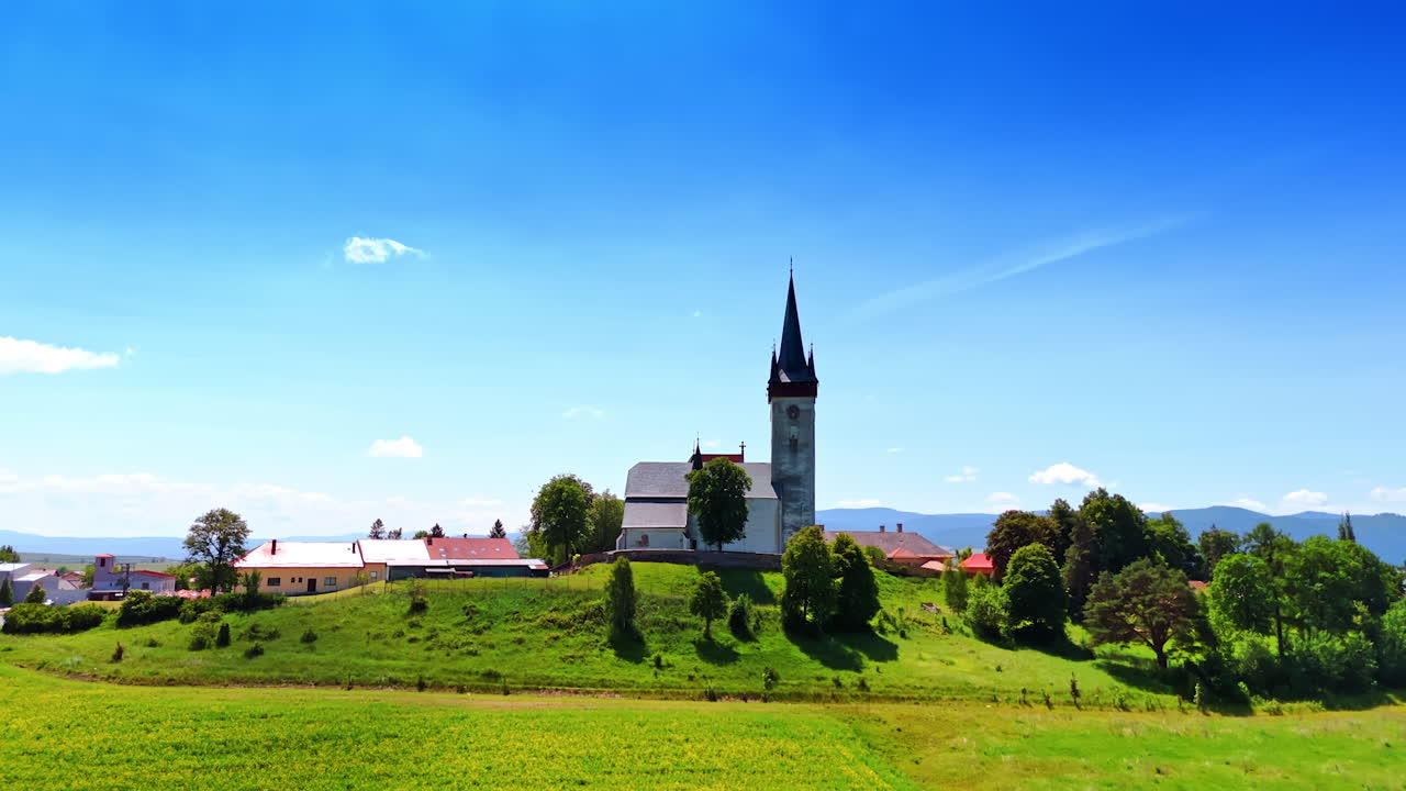 Approaching the old church with a long steeple. Picturesque countryside in Slovakia on sunny day