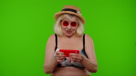 una anciana turista en traje de baño jugando a un videojuego en su teléfono móvil con una llave chroma.