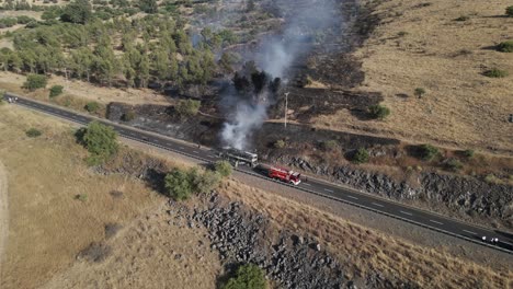 firetruck with water hose next to a burning passenger bus, drone pulling away