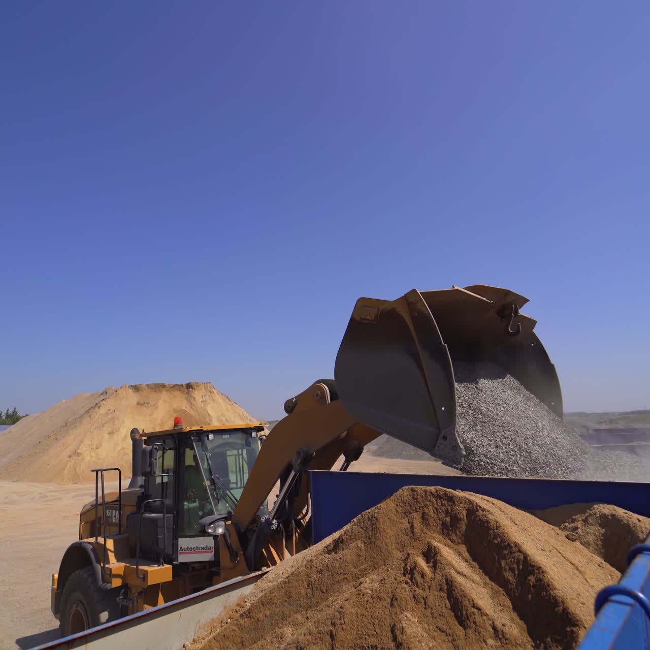 Outdoor plant for making new asphalt. Excavator pouring mixed asphalt. Manufacturing background at daytime.