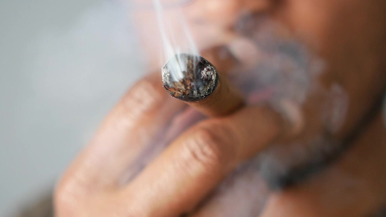 Primer plano de un hombre fumando un puro encendido con humo ascendente