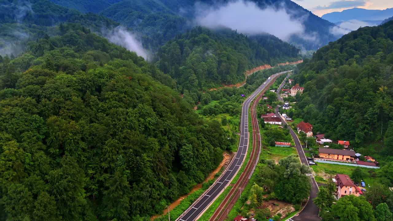 Winding mountain road view. Lush green mountains surround a curved road, with quaint houses nestled below during a misty morning scene