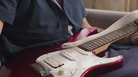 close-up van een onherkenbare man die op de bank zit met een elektrische gitaar en een slang over zijn benen