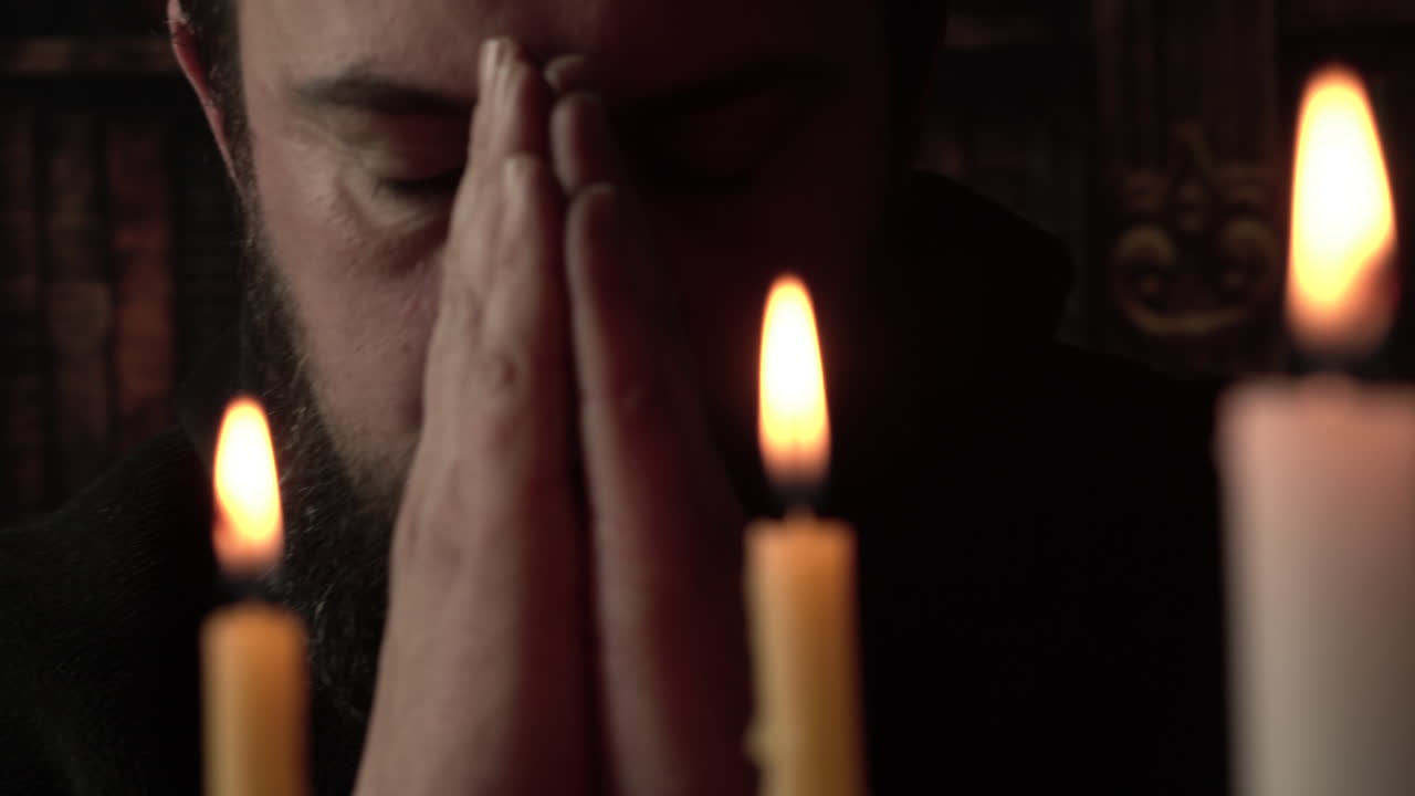 Uomo religioso in chiesa cattolica che si fa il segno della croce davanti alle candele, primo piano