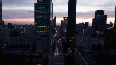 Downtown-skyscrapers-silhouettes-against-colourful-twilight-sky.-Forwards-fly-above-busy-multilane-road.-Warsaw,-Poland
