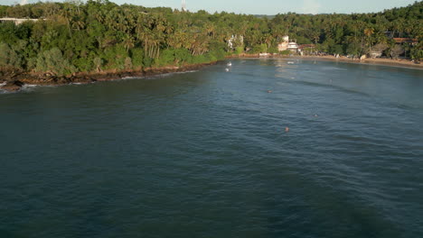 Establishing-Aerial-Drone-Shot-of-Hiriketiya-Beach-and-Bay-with-Surfers-in-the-Water