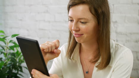 Eine-Glückliche-Junge-Frau,-Die-Ein-Tablet-Benutzt-Und-An-Einem-Schreibtisch-Sitzt