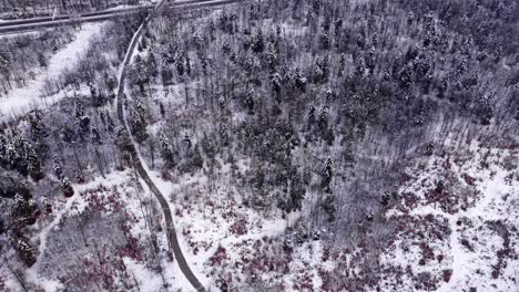 A-breathtaking-winter-journey:-A-wide-shot-drone-view-of-a-winding-uphill-road-through-a-snow-covered-forest,-leading-to-a-rural-European-highway