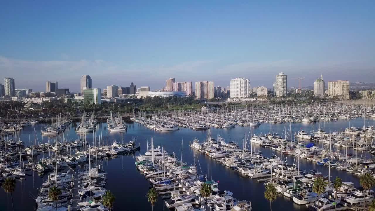 Aerial pan right of Shoreline Yachts docked on blue water near long beach and downtown skyline in background in los angeles