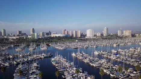 aerial pan right of shoreline yachts docked on blue water near long beach and downtown skyline in background in los angeles