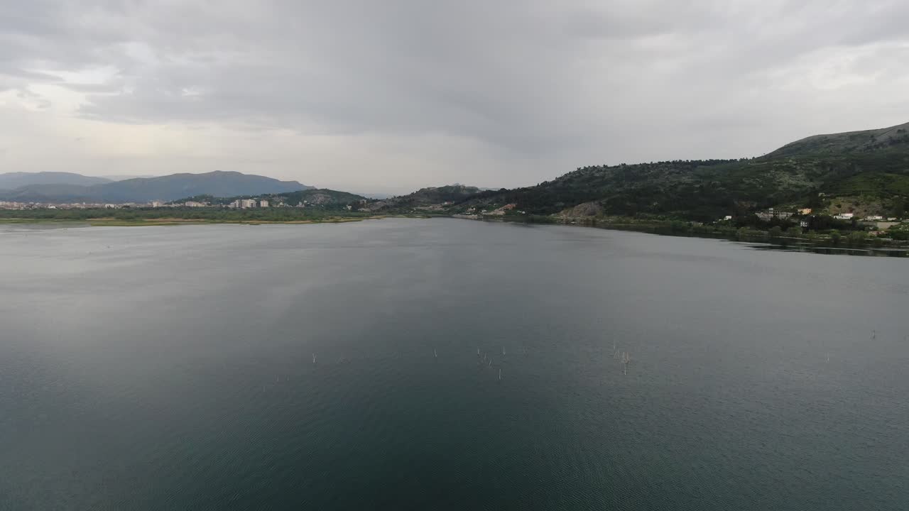 Drone view in Albania flying over Shkod&euml;r lake in Pogradec on cloudy day with mountains in the horizon