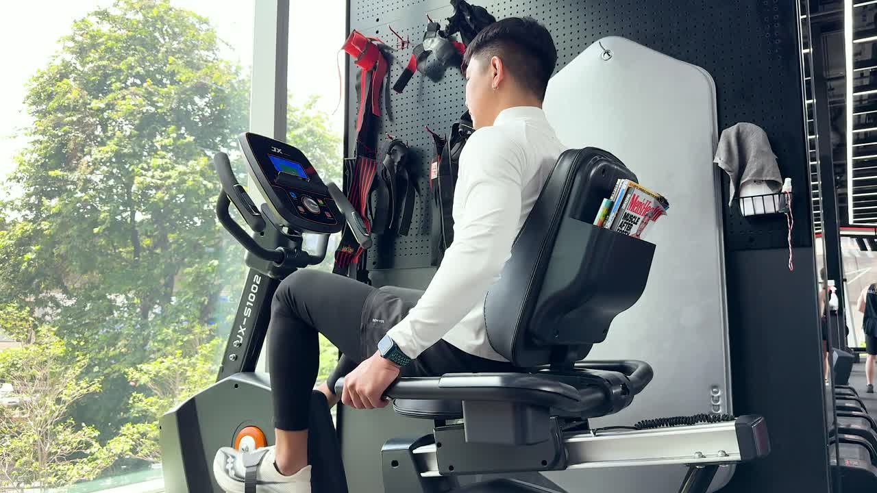 Man exercising on recumbent bike in modern, naturally lit gym, focusing on fitness and health