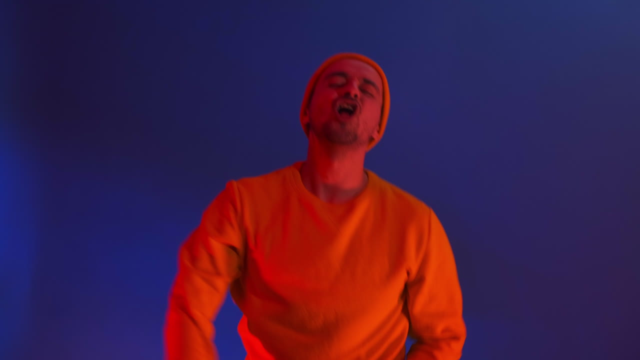 남자는 즐겁게 춤을 추고 스트로브 조명과 컬러 스포트라이트의 빛에 카메라를 바라본다. 네온 색과 미친 남자가 음악에 춤을 추고 노란색 재 ⁇ 과 모자를 입고 노래하고 있다.