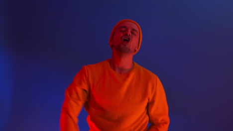 the man dances merrily and looks at the camera in the light of strobe lights and colored spotlights. neon colors and crazy man dancing to music and singing in a yellow jacket and hat