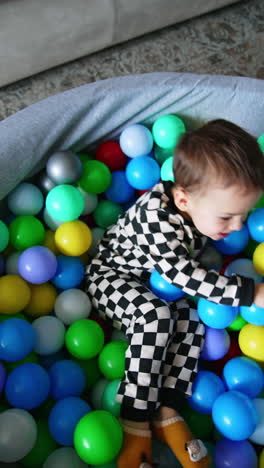 happy cheerful kid in checkered pajama sits in the dry pool. energetic toddler having fun time at home. top view. vertical video.
