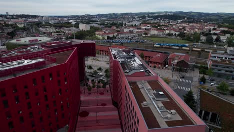 lateral-drone-shot-of-Saint-Etienne-Business-district-and-chateaucreux-train-station-on-an-overcast-day-with-red-building-in-the-foreground