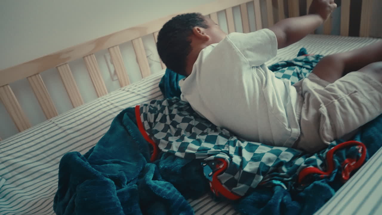 Black dad wrestles toddler son in bed while infant brother watches. Scene ends on close-up of toddler laughing with joy and connection