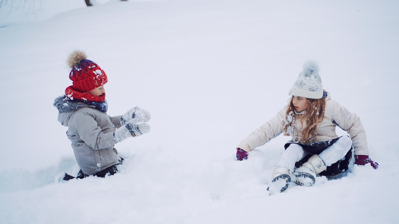 Beautiful children are standing out from white snow outdoors. Little girls on the snowy background in winter. Slow motion.