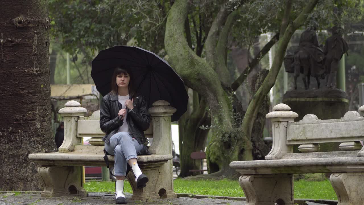 슬픈, 좌절 된 젊은 여성은 검은 우산 아래 공원의 벤치에 앉아