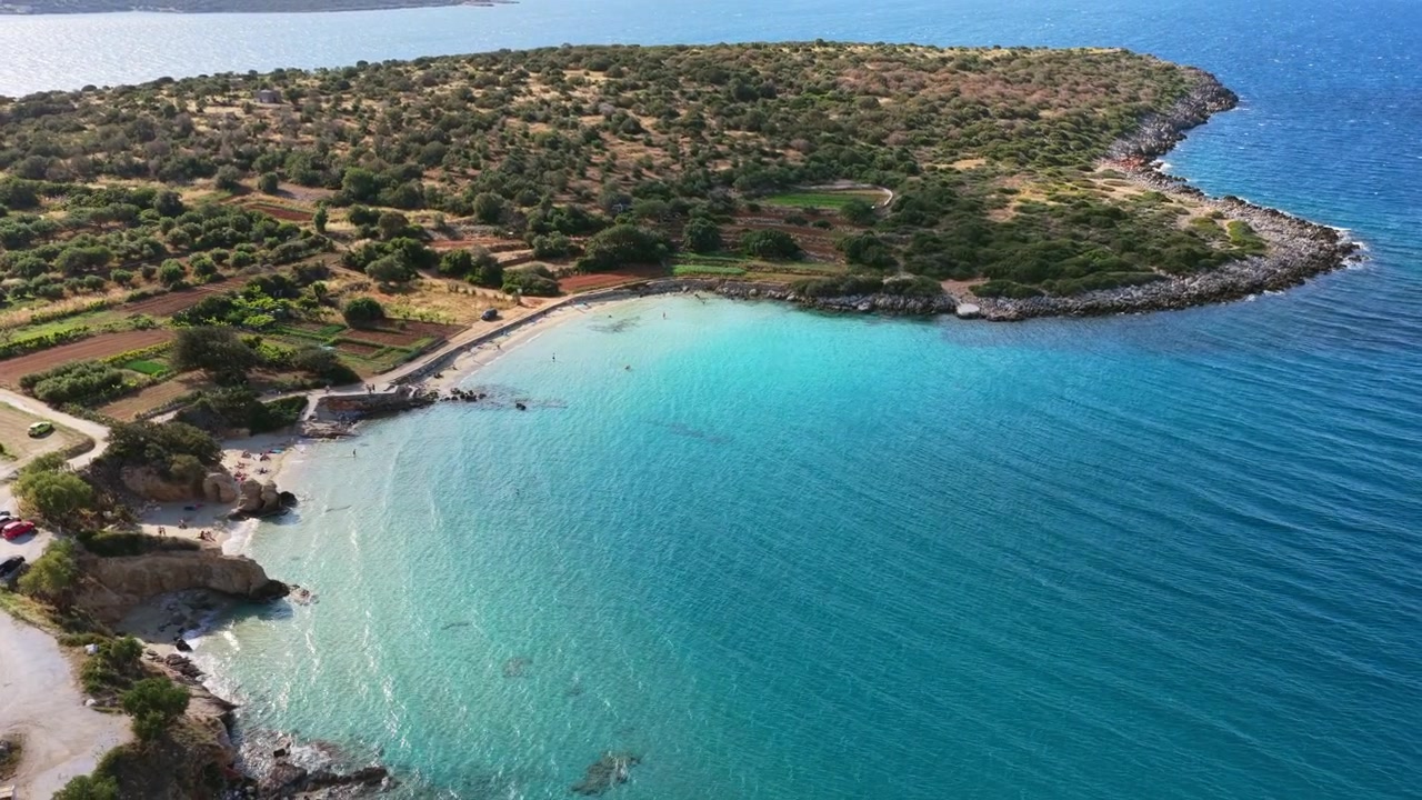 Vista aerea con drone di una penisola boscosa con una cala sabbiosa e turchese e un bar sulla spiaggia in una baia circondata da montagne, Spiaggia di Voulisma, Grecia