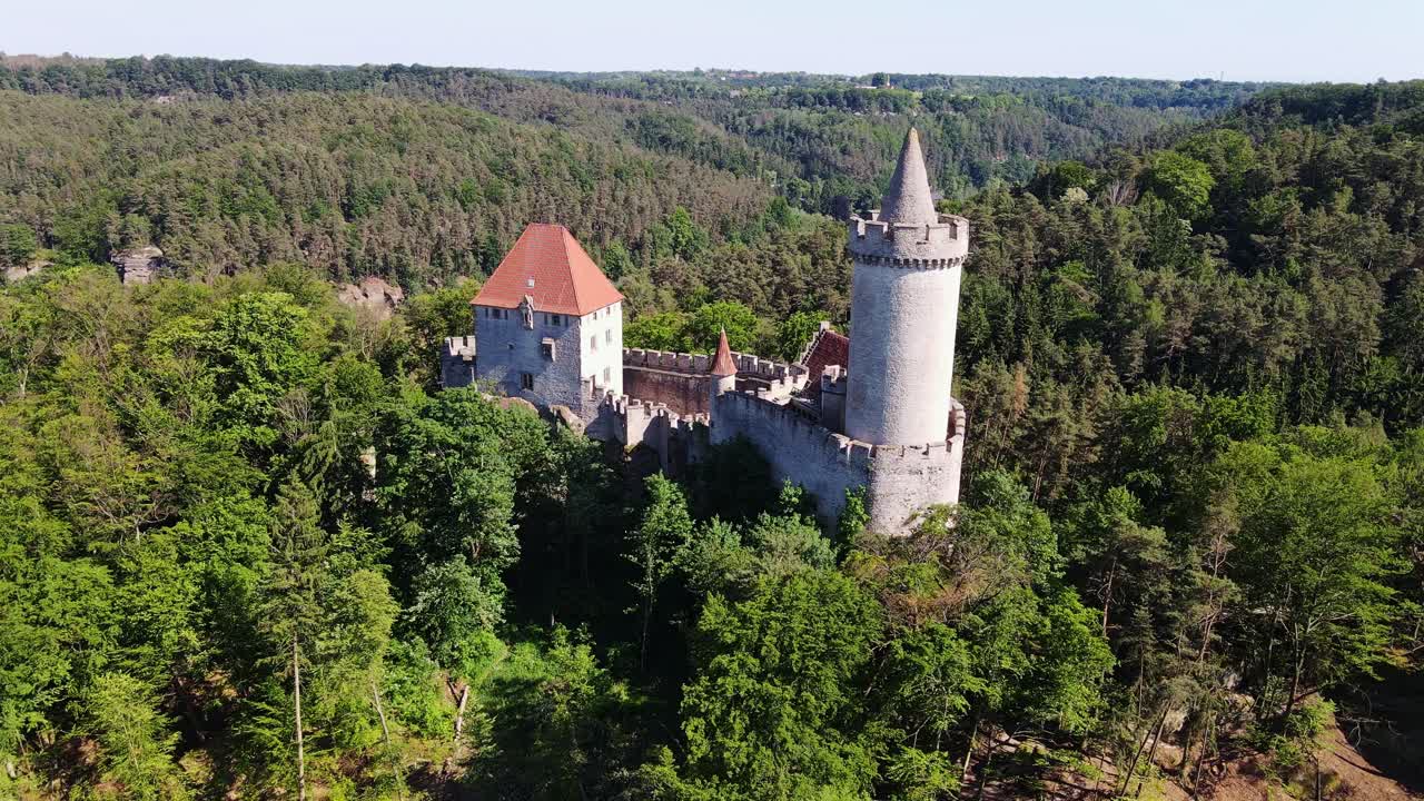 Drone fly over Kokořín Castle in Czechia, surrounded by rolling forested hills