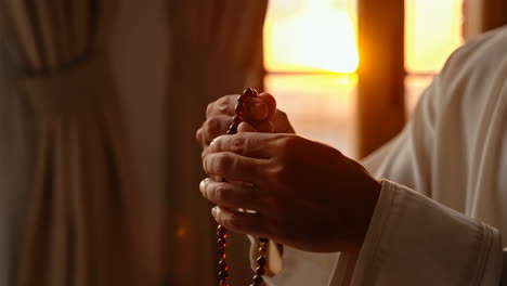 close-up of hands holding prayer beads during golden hour