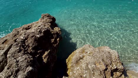 Cliffs-washed-by-crystal-seawater-on-rocky-beach-with-sand-at-sunrise-in-Mediterranean,-beautiful-summer-vacations