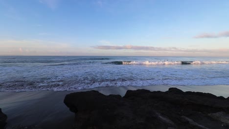 waves rolling in on beach at sunrise with large rock in the foreground