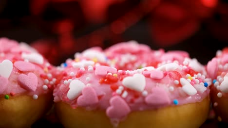 sprinkles falling onto pink donuts with heart shaped sprinkles - sliding shot